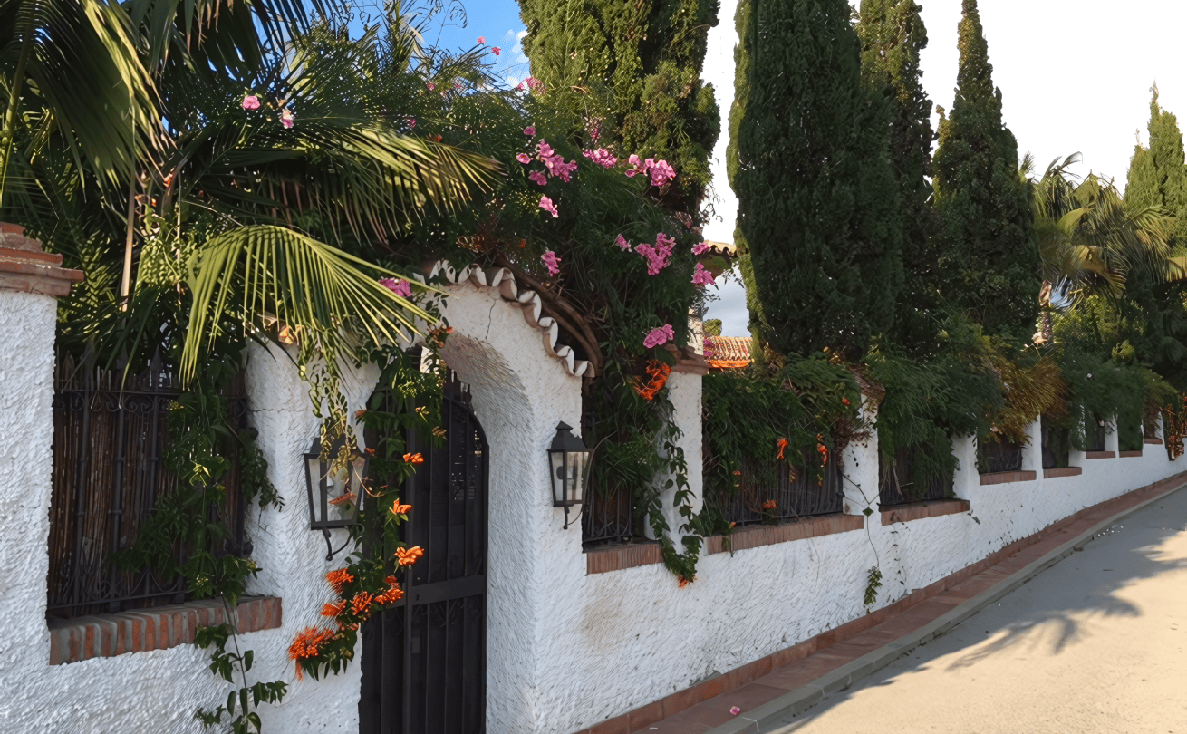 Majestic view of the Costa Bella coastal sanctuary with blooming bushes, ornate gates, and a wall adorned with live flowers.